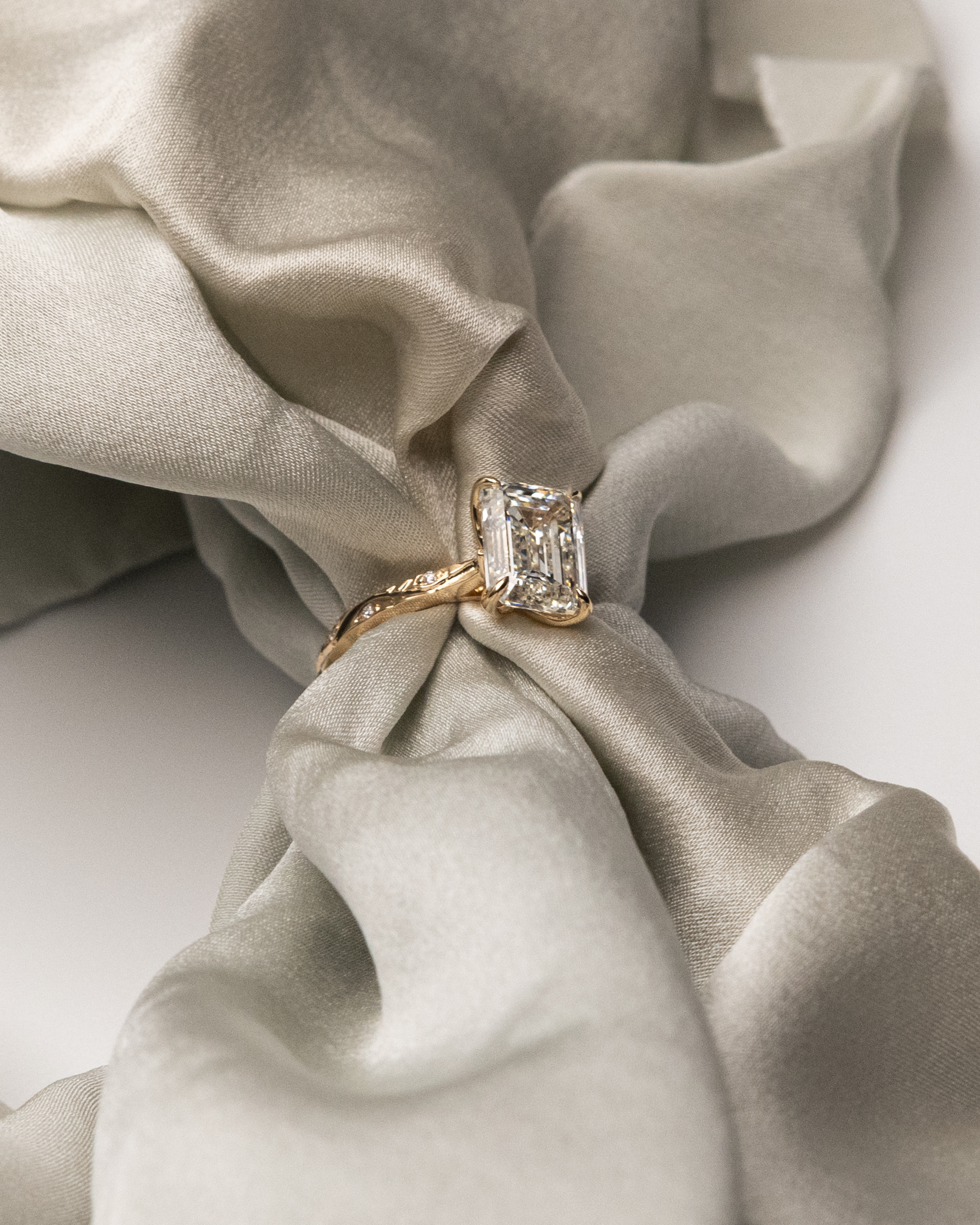Emerald cut diamond engagement ring in yellow gold resting on satin fabric — are lab grown diamonds real guide by Kalakari